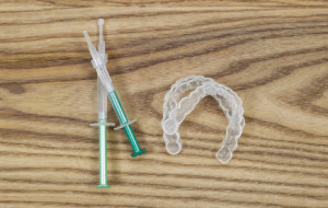 Overhead view of dental whitening trays and gel tubes on aged wood
